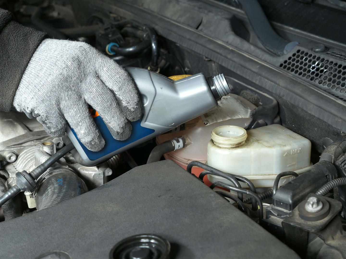 Close-up of a gloved hand pouring fresh engine oil to the tank